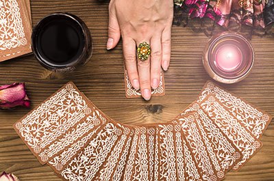 Female hands drawing a tarot card from a spread of cards, placed face down on a wooden table.